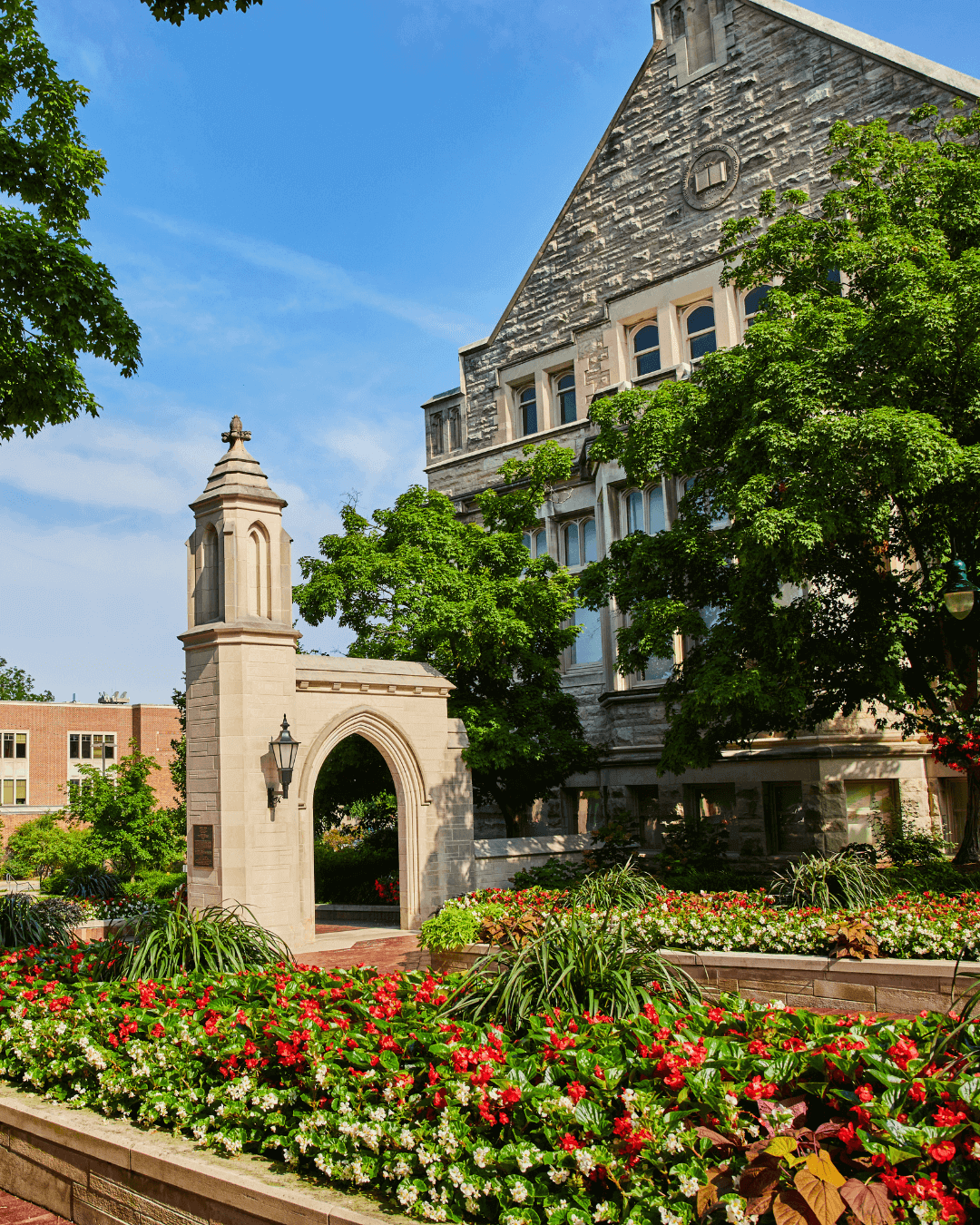 University-style stone building with arched entrance and landscaped flower beds in front